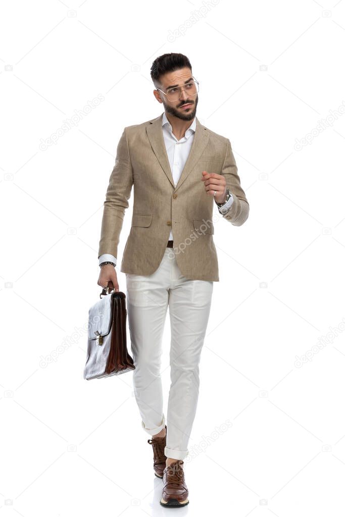 sexy businessman with style is walking with a briefcase in a hand and looking away on white background