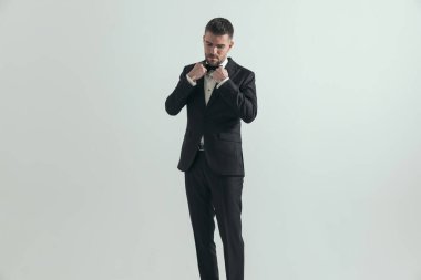 Seksi iş adamı papyonunu düzeltiyor, aşağı bakıyor ve gri arka plana karşı dramatik davranıyor.