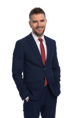 Genç yakışıklı adam elleri ceplerinde poz verirken rahatlamış hissediyor ve gülümsüyor.