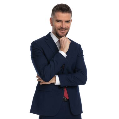 Çekici iş adamı nazikçe çenesine dokunuyor, kollarını kavuşturup kameraya gülümsüyor.