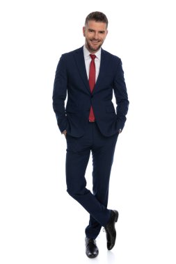 Çekici iş adamı rahat duruşu, bacak bacak üstüne atması ve beyaz arka planda kameraya gülümsemesi.