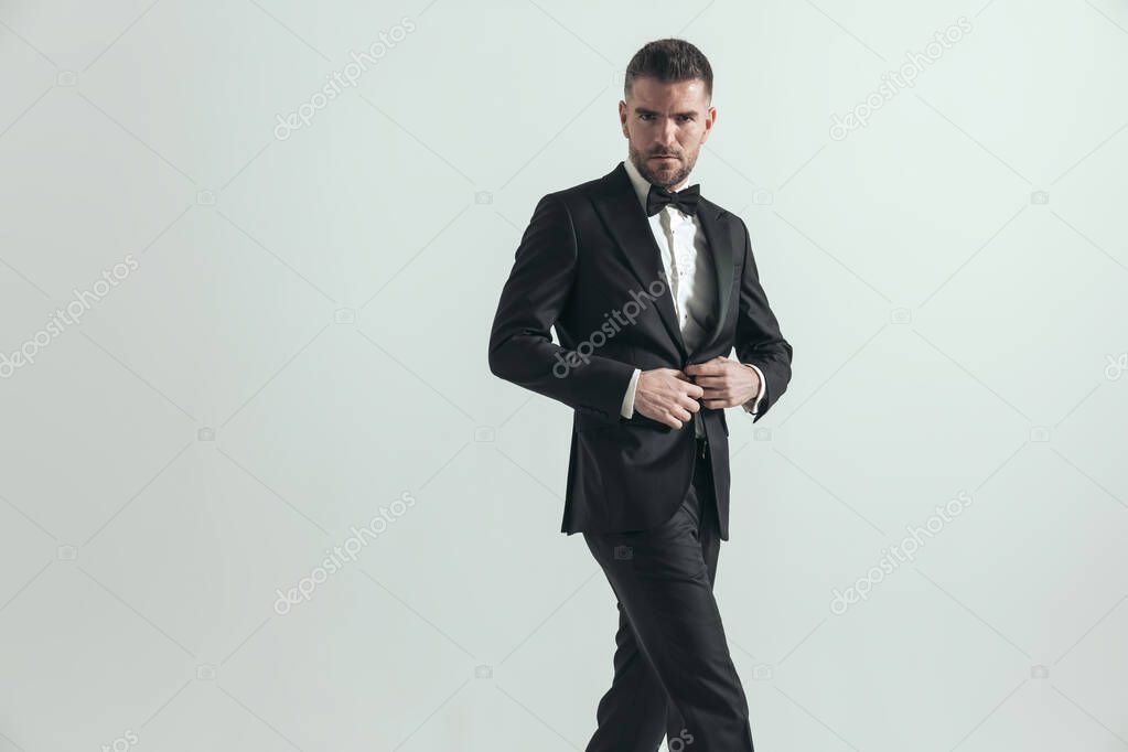 sexy businessman with a deep look on his face is closing his jacket, crossing his legs and posing 