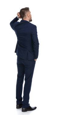 Kafasını kaşıyan bir iş adamının arkadan görünüşü ve bir elini cebinde tutarak bir kararı düşünmesi.