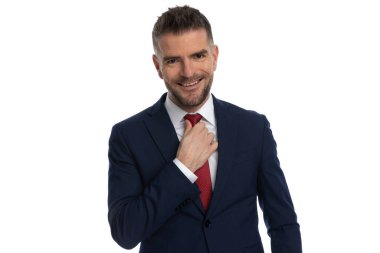 Havalı bir iş adamı geniş bir gülümsemeyle kravatını düzeltiyor ve bu seansta poz verirken iyi vakit geçiriyor.