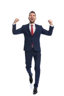 Genç işadamı kameraya doğru yürüyor ve beyaz stüdyo geçmişine karşı başarıyı kutluyor.