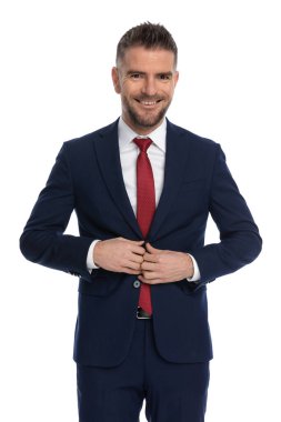 Mutlu iş adamı ceketini beyaz arka plana kapatırken kameraya gülümsüyor.