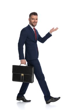 Bir iş adamının yürürken ve elinde bir çanta tutarken kameraya gülümserken bir yandan da bir şey sunarken yan görünümü