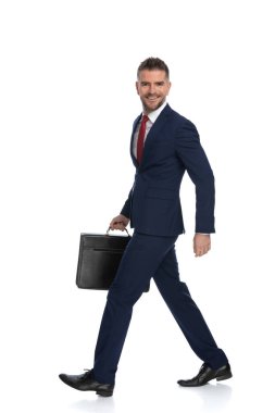 Yüzünde bir gülümsemeyle yürüyen bir iş adamının yan görünüşü ve bir elinde beyaz arka plana karşı açılan bir dava.