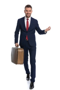 Çekici iş adamı yaz tatili için bizi selamlıyor, bir bavul tutuyor ve gülümsüyor.