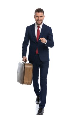 Mutlu iş adamı kameraya doğru yürür, parmağını gösterir ve beyaz sırtında bir valiz taşır.