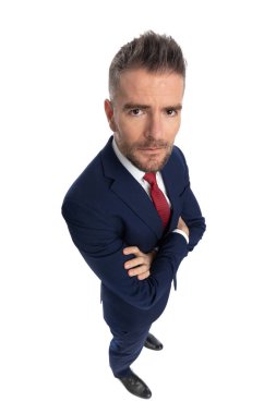 Ciddi bir iş adamının kollarını kavuşturup beyaz arka planda kameraya baktığı geniş açı.