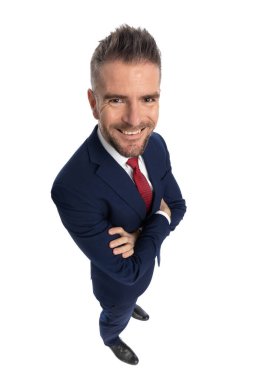 Geniş açılı genç bir iş adamı kollarını kavuşturup kameraya gülümsüyor beyaz arka planda.