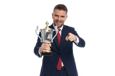 Yakışıklı iş adamı kamerayı işaret ediyor ve beyaz arka plana karşı bir bardak kaldırıyor.