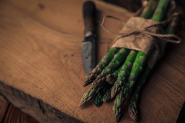 Yaya bağlanmış taze kuşkonmaz. Eski bir doğrama tahtasındaki bıçakla doğramaya davet edilmiş.