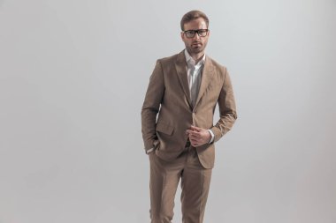 Yakışıklı iş adamı ceketini açıyor ve bir elini gri arka plana sokuyor.