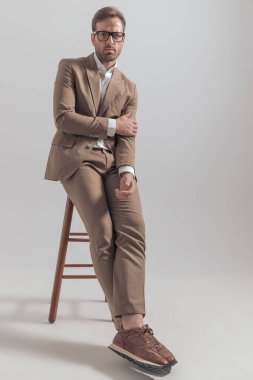 Genç yakışıklı iş adamı kolunu tutuyor, ayaklarını çapraz tutuyor ve gözlük takıyor. 