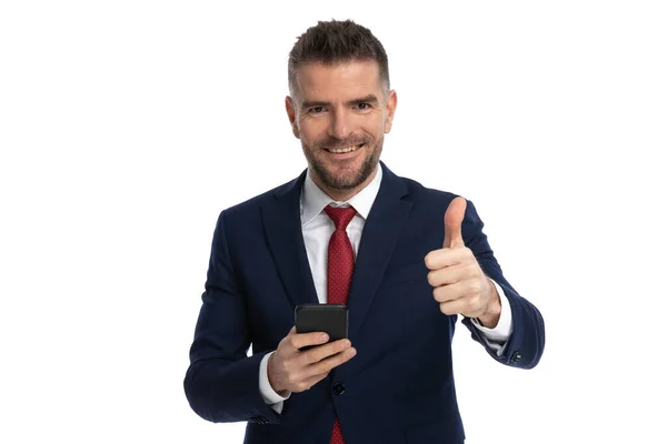 魅力的なビジネスマンが親指を立てて携帯電話を持ちカメラで微笑んだ — ストック写真