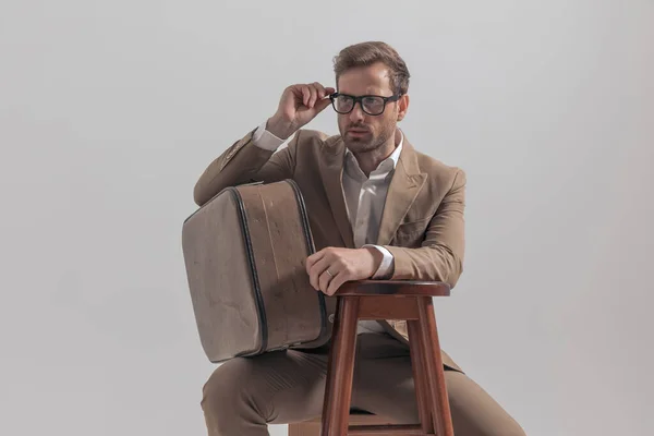 Genç Yakışıklı Adam Gözlüklerini Ayarlıyor Bavulunu Tutuyor Gri Arka Planda — Stok fotoğraf