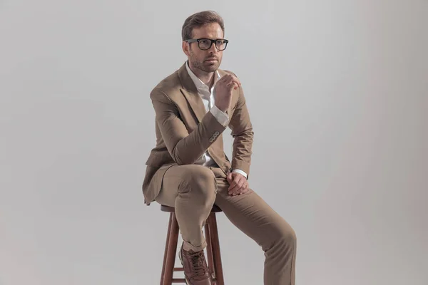 彼の膝の上に彼の手で椅子に座って 灰色の背景を前に見てクールなビジネスマン — ストック写真