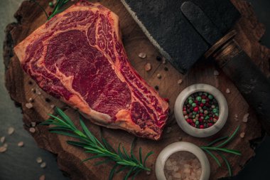 Biyografinin üst kısmındaki pişmemiş kırmızı bifteği biberiye, renkli biber, pembe tuz ve eski ahşap kesim tahtasının tepesinde satır bıçağıyla kapatın.