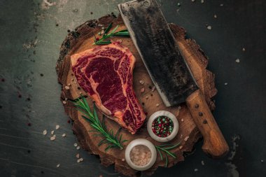 Üstünde çiğ et, satır bıçağı, kırmızı ve yeşil biber, pembe tuz ve biberiye olan klasik kesim tahtasının estetik sunumu