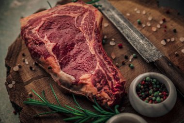 Bifteğin eski bir vintage kesim tahtasının tepesinde mutfak bıçağı, otlar, tuz ve biberle pişirildiği yakın plan fotoğrafı.