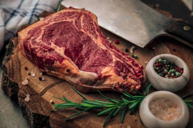 Küçük kaseler dolusu pembe tuz, renkli biber ve ahşap doğrama tahtasının üzerinde satır bıçağı olan çiğ sığır eti sunumunu kapat.