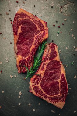 İki parça pişmemiş biftek, biberiye ve demir masanın üstüne tuz ve biber serpiştirilmiş.