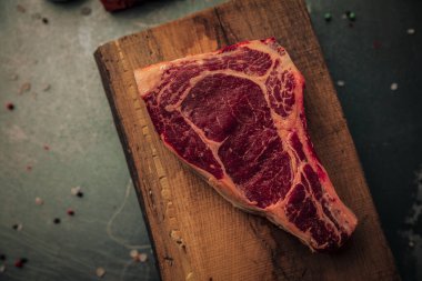 table top of uncooked red meat on top of old rustic chopping board with some sprinkles of salt and pepper around on iron table