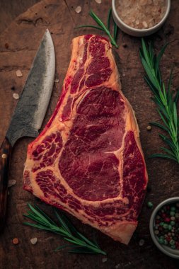 Üstünde et olan ahşap doğrama tahtasının üst görüntüsü, biberiye otları, tuz ve biber kaseleri ve mutfak bıçağı lezzetli bir akşam yemeği için hazır.