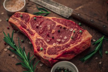 Pişmemiş taze biftek, tuz, biber ve yeşil baharat serpiştirilmiş. Köy ahşap kesme tahtasının tepesinde bıçak, kase tuz ve biber var.