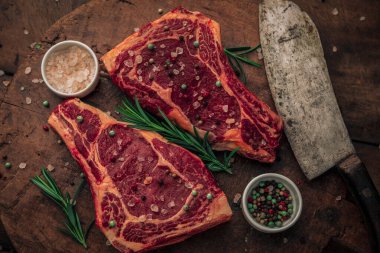 Kırmızı biftek, tuz ve biber serpintileri, biberiye, satır bıçağı ve bir kase himalaya pembe tuzu ve renkli biber içeren estetik resim.