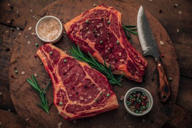 Mutfak bıçağının yanına yeşil otlar ve tuz ve biber serpiştirilmiş estetik kırmızı et manzarası ve ahşap kesim tahtasının üzerinde tuz ve biber kaseleri.