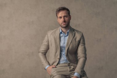 Genç yakışıklı işadamı bir elini cebine koydu ve duvar kağıdına karşı sıkı bir duruşla poz verdi.