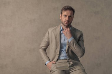 Yakasını düzenleyen çekici bir iş adamı, bir elini cebine koyar ve duvar kağıdına yaslanır.