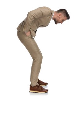 Orta yaşlı, bej takım elbiseli, el ele tutuşmuş, aşağıya bakıp beyaz arka planda çok küçük bir şey görmeye çalışan adamın yan görüntüsü.