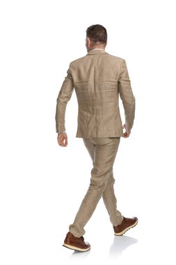 Takım elbiseli ve spor ayakkabılı bir adamın arka plandaki beyaz arka planda yürüdüğünü gösteren bir fotoğraf.