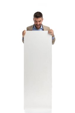 hapyp man in his 40s looking down while covering body with empty board and making shocked face on white background in studio