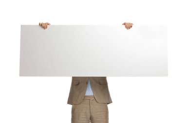 man in beige suit covering face with empty white board on white background in studio