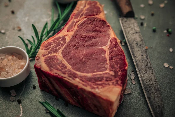 Demir masa, üzerinde pişirilmemiş biftek, tuz ve biber serpintileri ve bıçak ve bir kase himalaya pembesi.