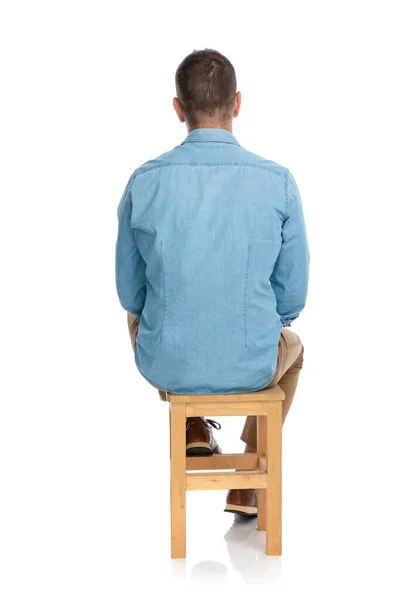 在演播室里 穿着牛仔衬衫的便衣人员坐在白色背景前的木制椅子上的后视图 — 图库照片