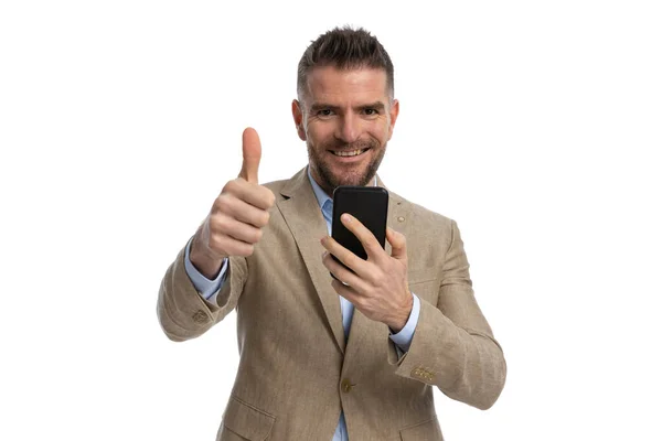 一个40多岁的英俊男子的画像 手里拿着手机 大拇指翘起 在白色的背景面前微笑 — 图库照片