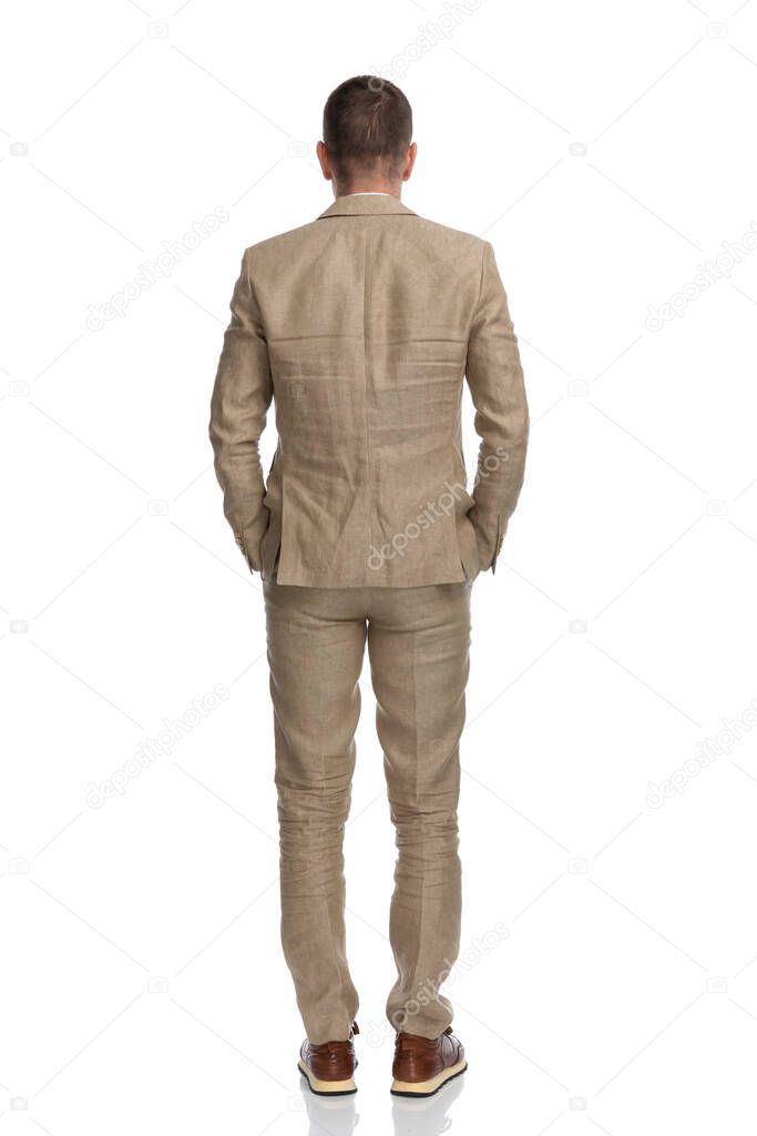 rear view of middle aged businessman with hands in pockets standing on white background in studio