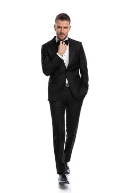 Seksi maço işadamı yüzünde sert bir ifadeyle yürüyor, papyonunu düzeltiyor, bir elini cebinde tutuyor. 