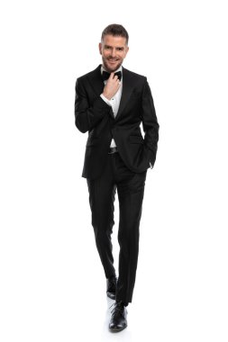 Zarif iş adamı papyonunu düzeltirken bir eli cebinde kameraya doğru yürüyor ve gülümsüyor.