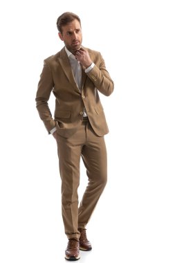 Havalı iş adamı bir eli cebinde yürüyor ve beyaz arka planda yakasını düzenliyor.