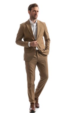 Havalı bir havası olan seksi iş adamı ceketini açarken ve moda pozunda elini cebinde tutarken yürüyor.