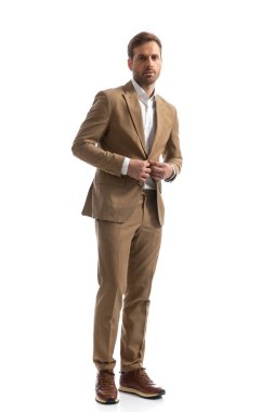 Genç yakışıklı iş adamı kahverengi takımını kapatıyor ve beyaz stüdyo geçmişine karşı poz veriyor.