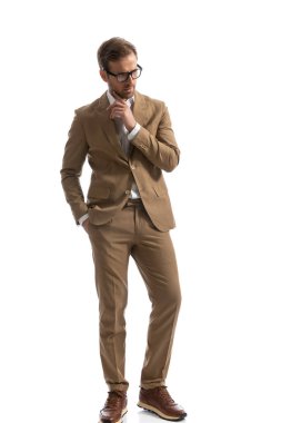 Yakışıklı iş adamı yavaşça çenesine dokunuyor, elini cebine atıyor ve başka tarafa bakıyor. 