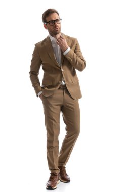 Çekici iş adamı yakasını düzeltiyor, bir elini cebinde tutuyor, yürüyor ve başka tarafa bakıyor. 